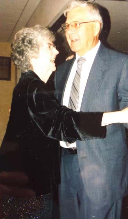 gray haired woman in black dress dancing with her gray haired husband in a gray suit