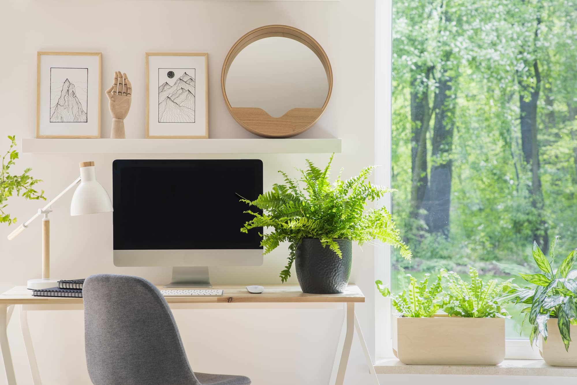 Grey chair at desk with plant in bright home office interior with window and posters. Real photo